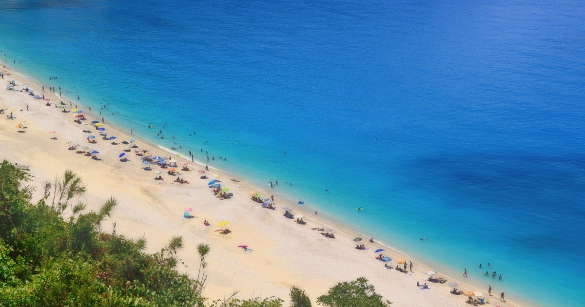 Turiști pe o plajă din Grecia, cu umbrele și șezlonguri