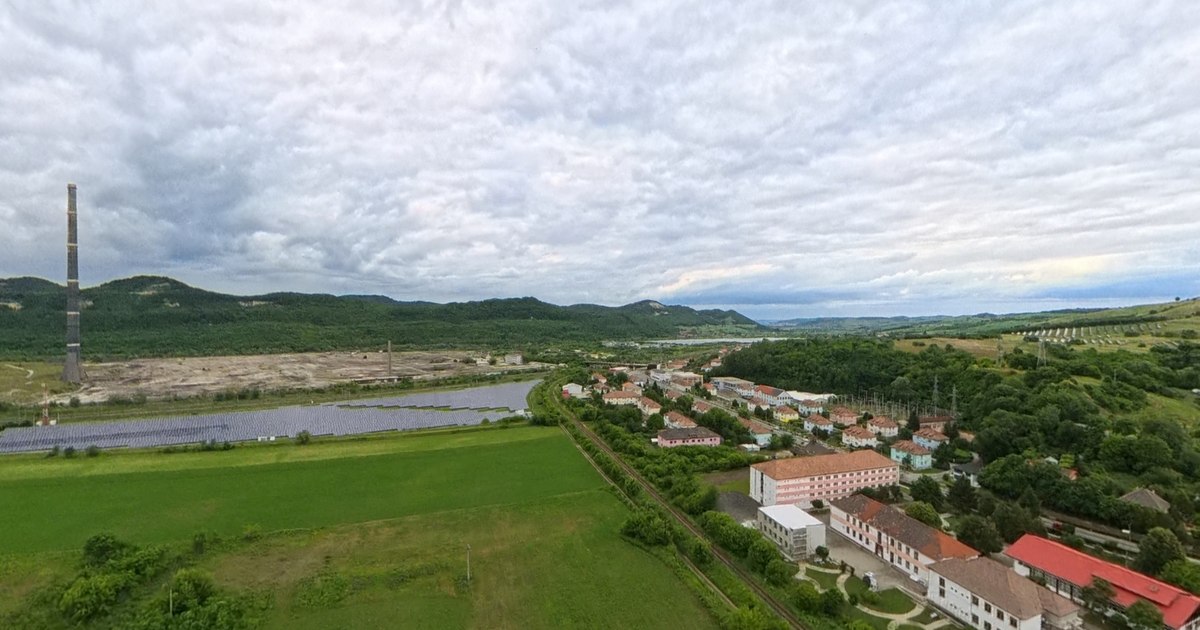 Vedere panoramică a orașului Copșa Mică, cu vegetație verde și coșul de dispersie al fostei uzine Sometra în fundal
