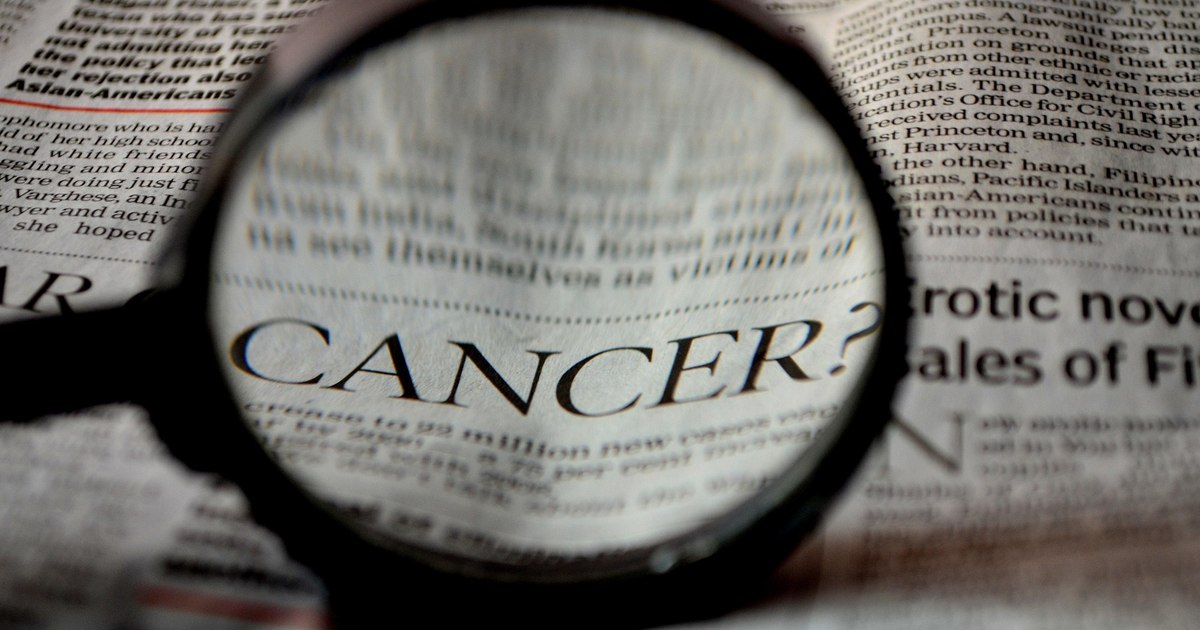O femeie cu bandană pe cap, simbol al pacienților oncologici, privind un telefon cu rețele sociale
