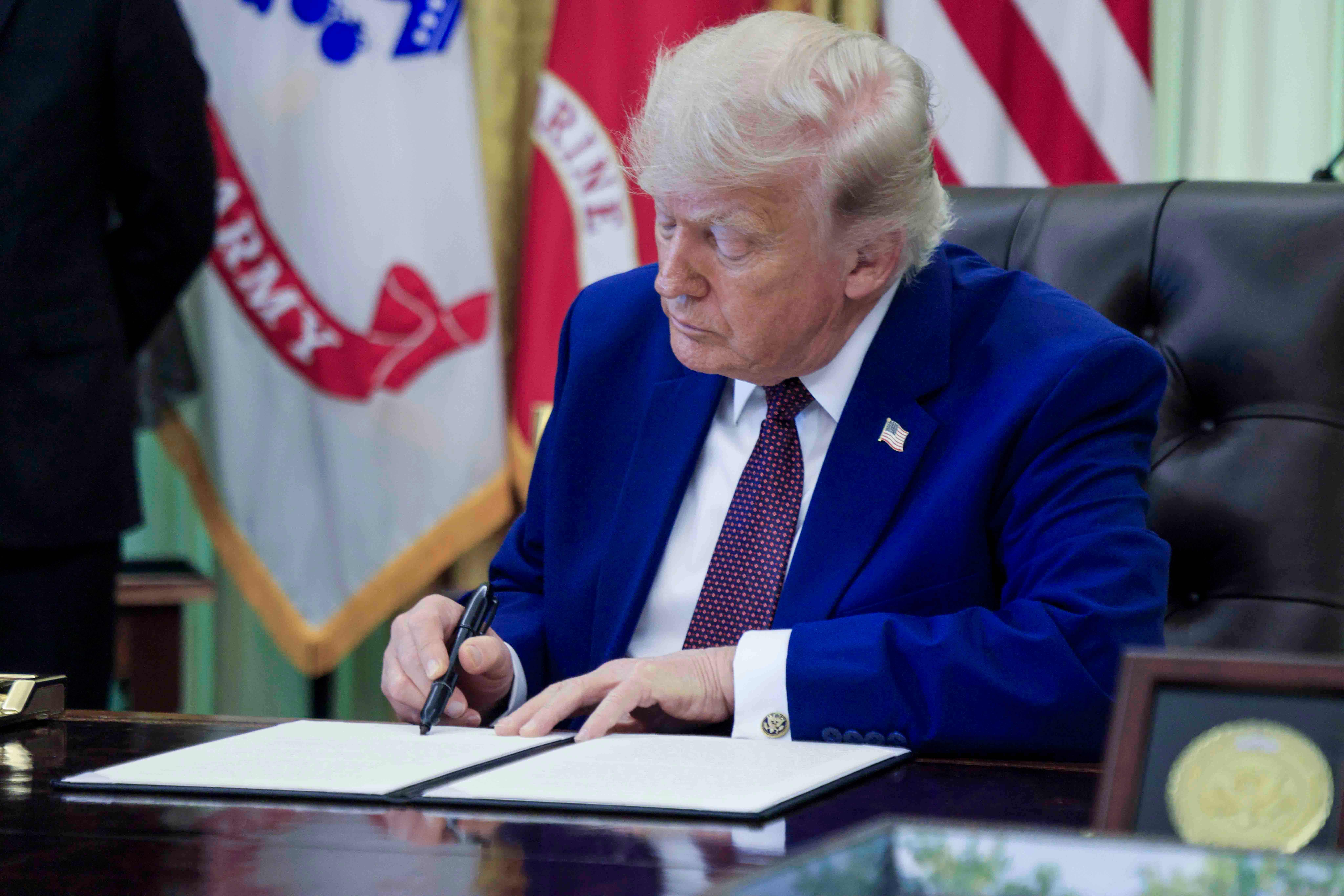 Donald Trump semnează un document la masa de lucru