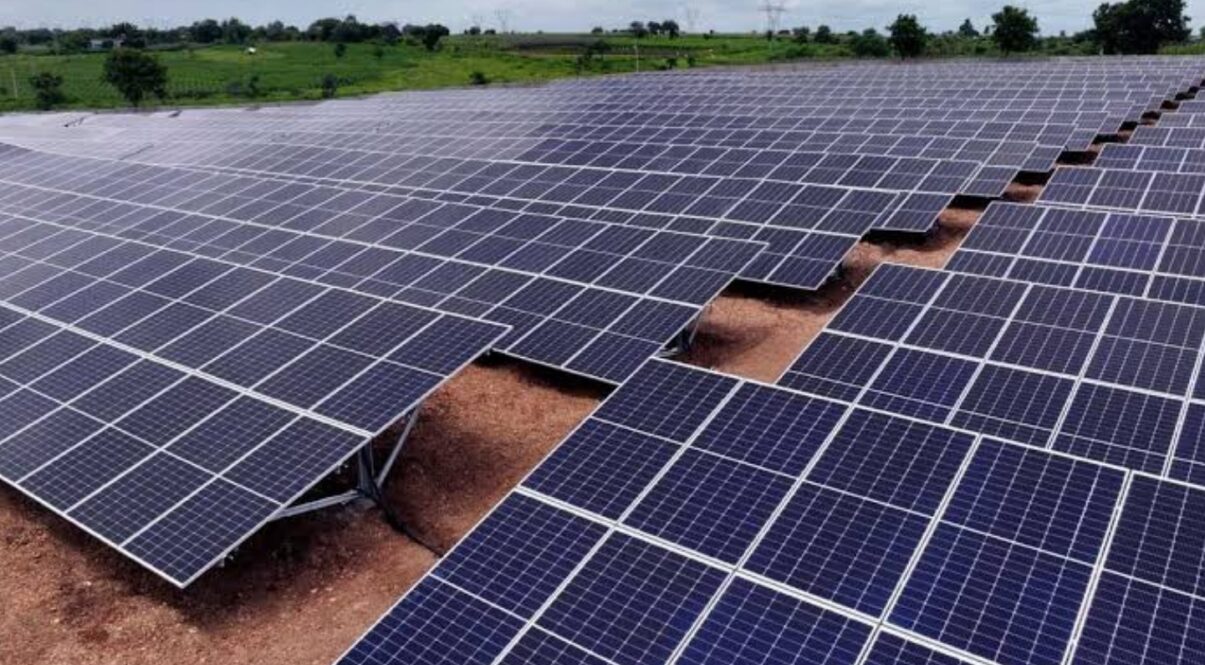 Panouri solare pe un câmp, cu cer albastru și nori