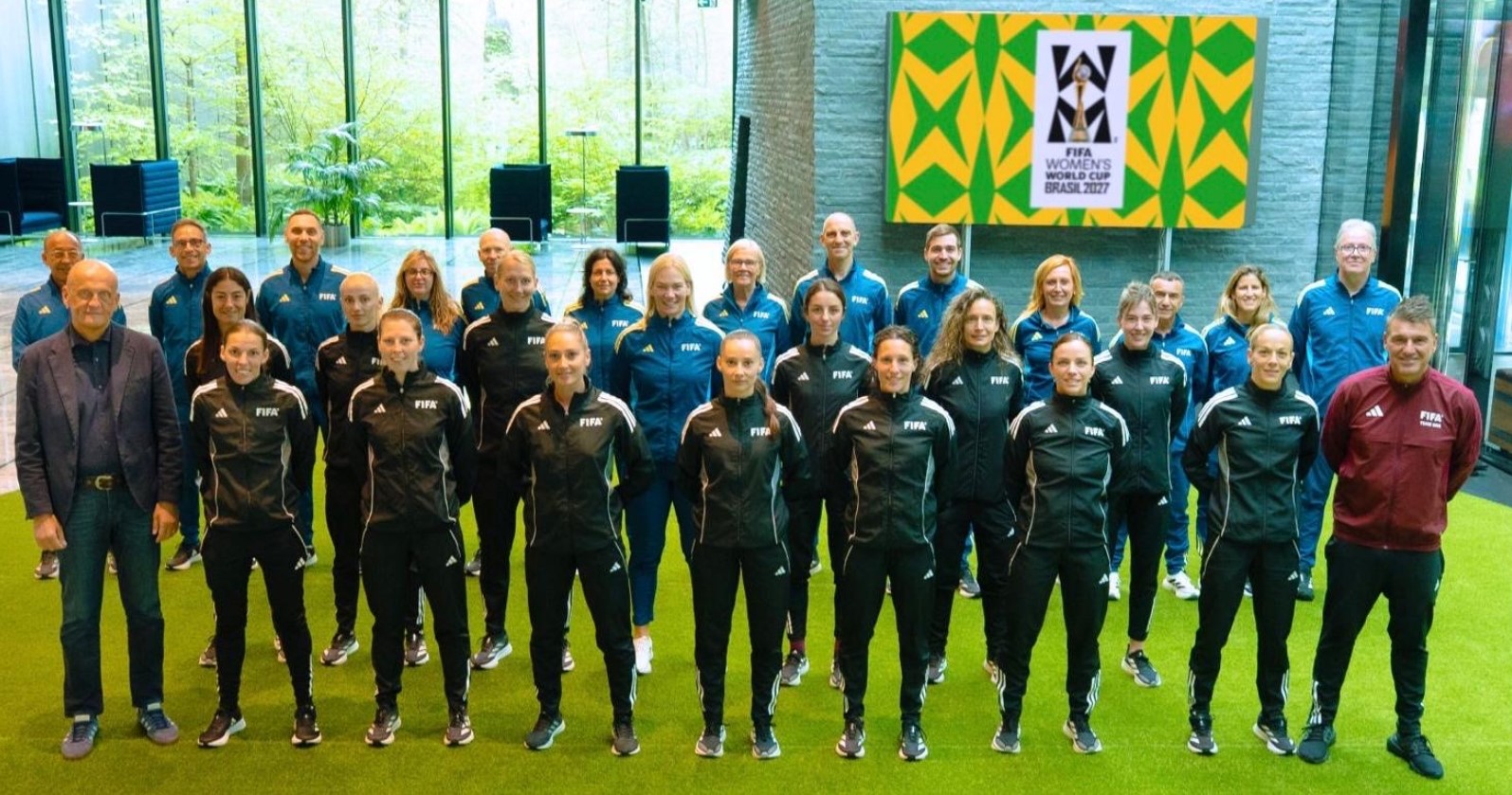 Arbitre de fotbal pe teren, cu steagul FIFA în fundal