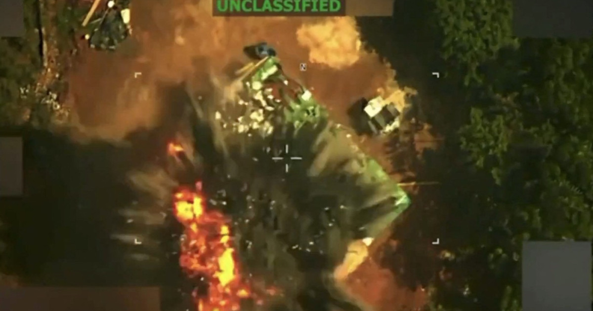 Imagine dintr-un videoclip care arată o clădire cu acoperiș verde înconjurată de vegetație, urmată de o explozie și un nor gros de fum