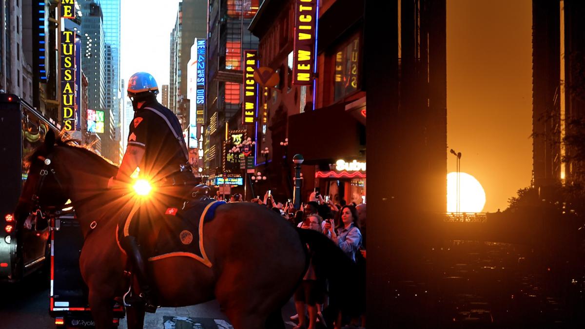Apus de soare portocaliu între zgârie-norii din Manhattan, cu oameni pe străzi fotografiind fenomenul Manhattanhenge