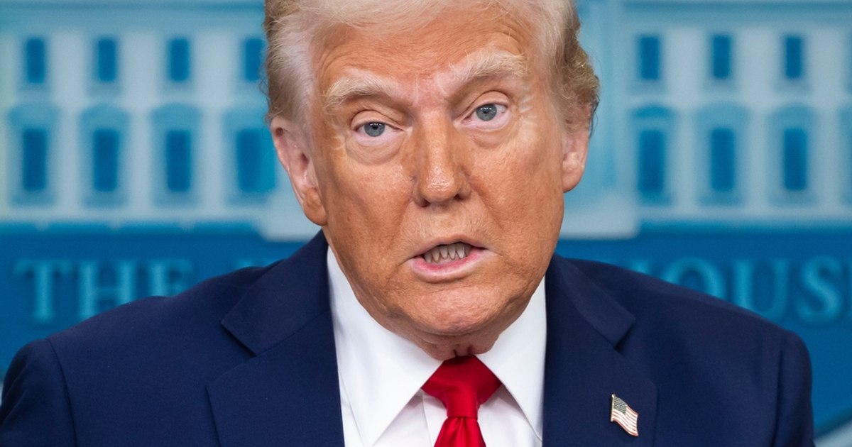 Donald Trump vorbind la un microfon, cu steagul american în fundal